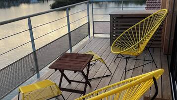 A wooden deck with yellow chairs and a table overlooking a body of water.