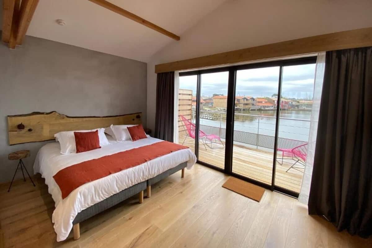 A bedroom with a large bed, a wooden headboard, and a view of a balcony with chairs.