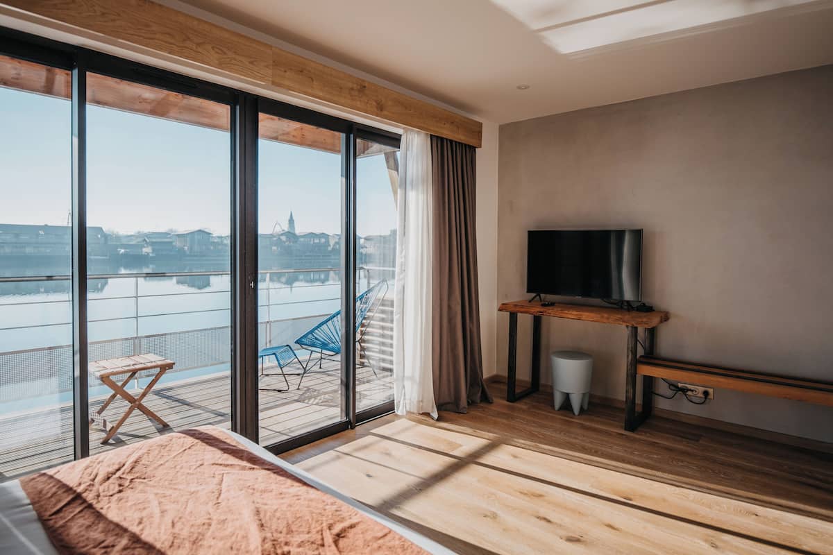 A modern hotel room with a large sliding glass door leading to a balcony with a view of the city.