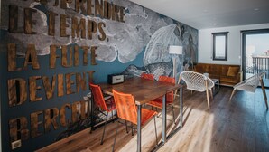 A modern dining area with a wooden table, orange chairs, and a mural with French text. - LES 12 DE LARROS (Gujan-Mestras)