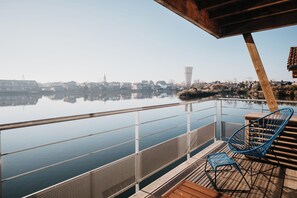 A wooden deck with a railing overlooking a calm body of water, a chair, and a small table. - LES 12 DE LARROS (Gujan-Mestras)