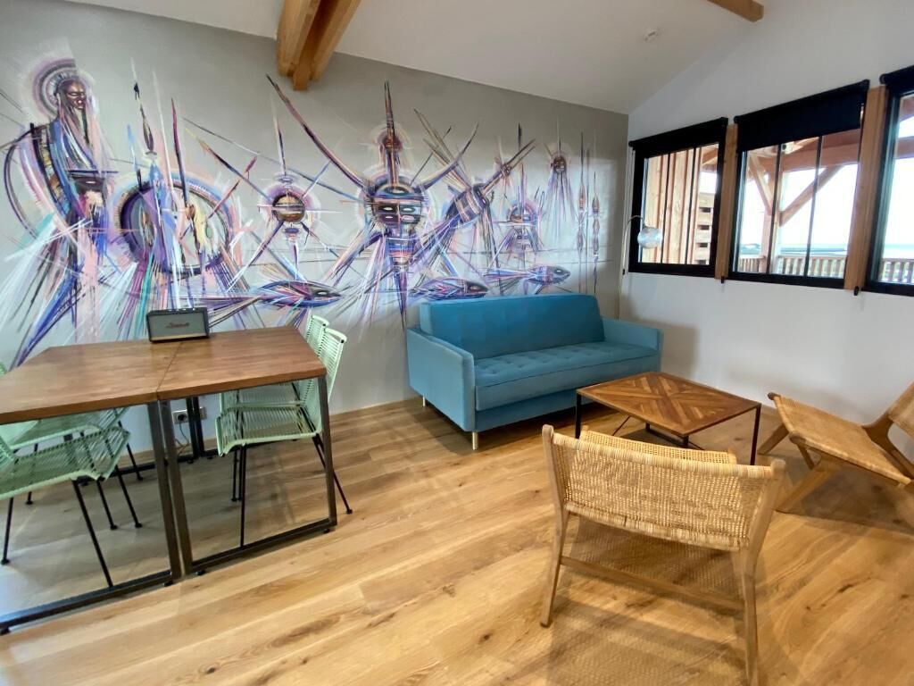 A modern living room with a blue sofa, a wooden dining table with chairs, and a large abstract mural on the wall.