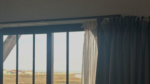 A window with vertical bars and a view of a landscape with fields and a distant building. - LES 12 DE LARROS (Gujan-Mestras)