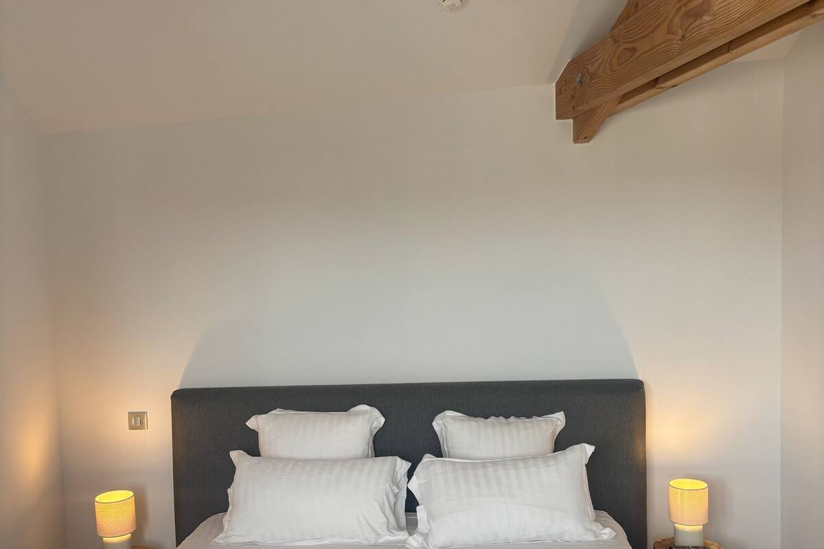 A neatly made bed with white linens, two bedside lamps, and a wooden headboard.