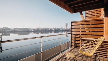 Una terraza de madera con barandilla que da a una masa de agua tranquila, una silla y una pequeña mesa.