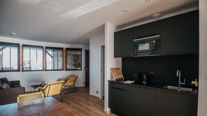 A modern kitchen with dark cabinetry, a microwave, and a sink. There is a wooden dining table with chairs in the adjacent living area. - LES 12 DE LARROS (Gujan-Mestras)