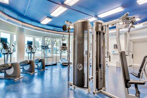 Une salle de sport équipée de divers appareils d’exercice, d’un grand miroir et d’une fenêtre laissant entrer la lumière naturelle.