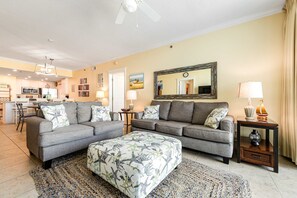 A modern living room with a grey sofa set, a patterned ottoman, and a dining area in the background. - Spacious Condo At Waterscape Lovely Gulf Views Playground, 2 Hot Tubs (Fort Walton Beach)