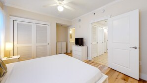 Une chambre d’hôtel avec un grand lit, un ventilateur de plafond, un téléviseur posé sur une commode et des portes blanches donnant sur d’autres chambres.