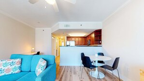 Un salon moderne avec un canapé de couleur turquoise, une table à manger avec des chaises, et un coin cuisine en arrière-plan.