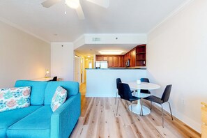 Un salon moderne avec un canapé de couleur turquoise, une table à manger avec des chaises, et un coin cuisine en arrière-plan.