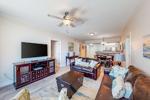 A living room with a dark brown leather sofa, a matching ottoman, and a flat-screen TV on a wooden entertainment unit. - Second floor beachfront condo with pool and hot tub access, w&D, and central AC (Fort Walton Beach)