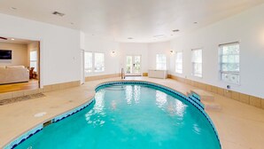 An indoor swimming pool with clear blue water, surrounded by white walls and a beige floor. - Two-story getaway with an indoor pool, patio, washer/dryer, & central AC (Panama City Beach)