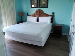 A hotel room with a large bed, a nightstand, a lamp, and two wall-mounted paintings. - Beautiful corner condo with Gulf & bay views, balcony, pool & hot tub (Panama City Beach)