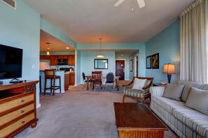 A living room with a television, sofa, coffee table, and dining area with chairs and a table. - Beautiful corner condo with Gulf & bay views, balcony, pool & hot tub (Panama City Beach)