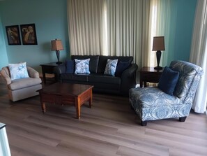 A living room with a sofa, armchair, and coffee table. - Beautiful corner condo with Gulf & bay views, balcony, pool & hot tub (Panama City Beach)