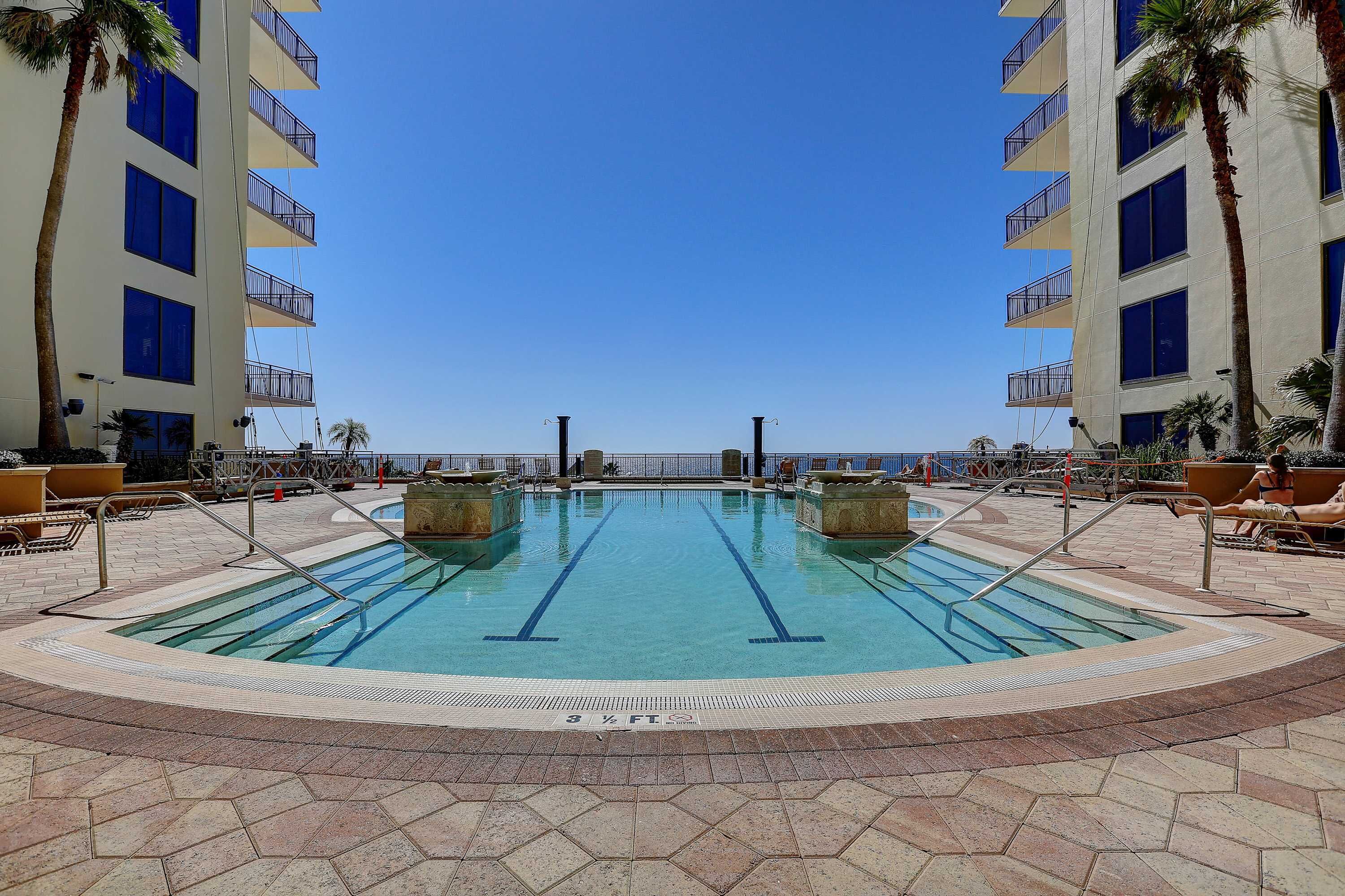 A swimming pool with two lanes, surrounded by palm trees and a view of the ocean.