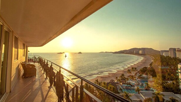 A balcony with a view of a beach and ocean during sunset. - Bay View Grand Residencial 11th floor (Ixtapa Zihuatanejo)