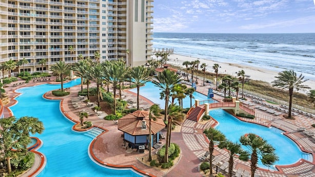 Ein Resort mit mehreren Swimmingpools, einem Strand und einem hohen Gebäude im Hintergrund.