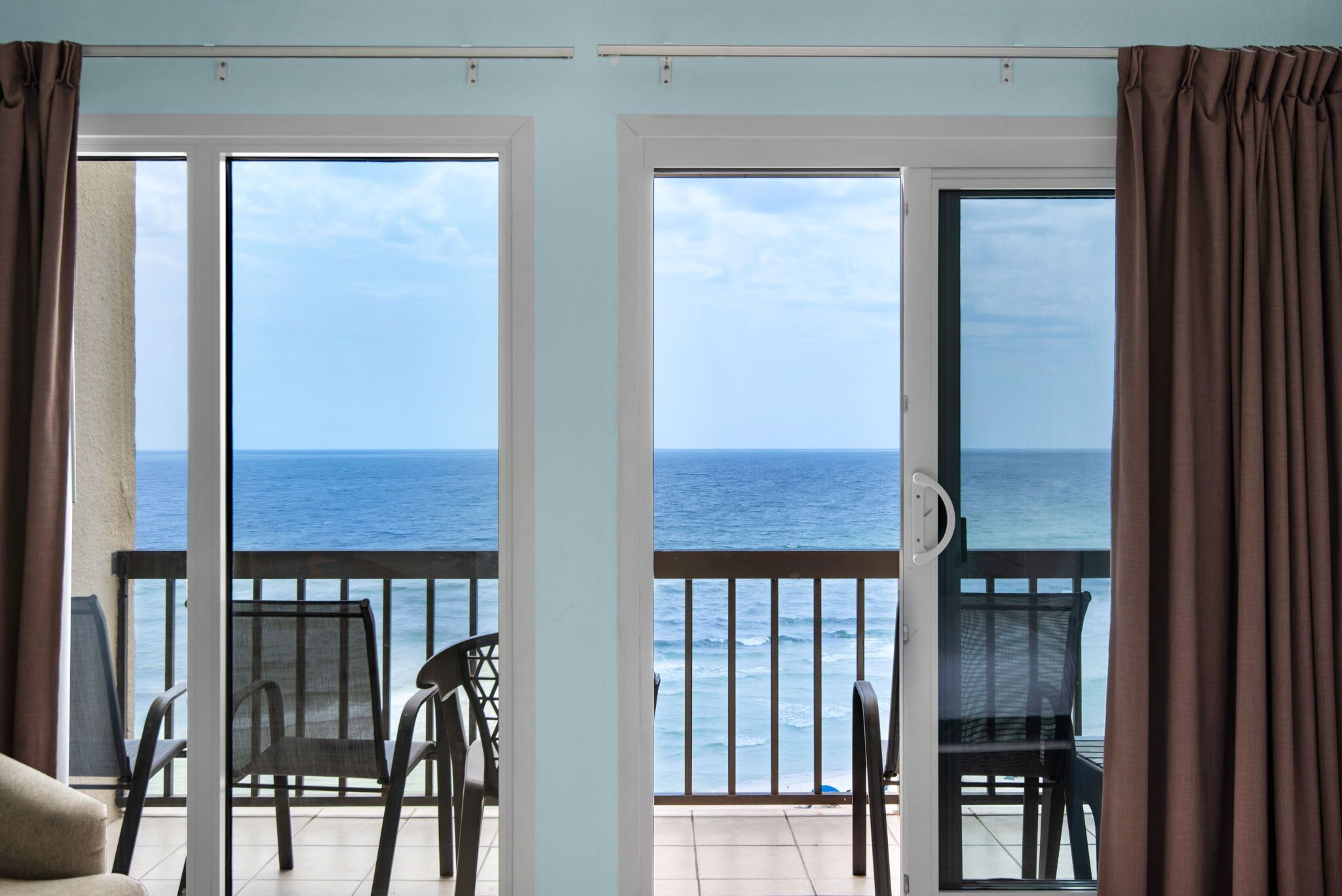 A room with a view of the sea through open sliding doors, a chair, and a table.