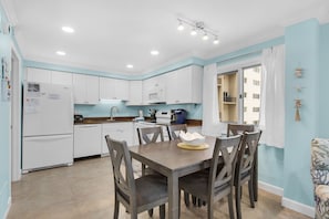 A modern kitchen with white cabinets, a dining table with chairs, and a window with curtains. - Oceanfront Pinnacle Port condo with tennis & basketball courts, private balcony (Panama City Beach)