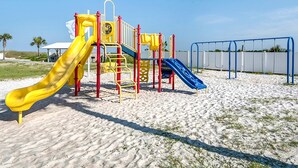 En legeplads med to rutsjebaner og en klatrestruktur på sand.