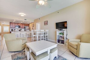 A spacious living room with a dining area, a kitchen in the background, and a flat-screen TV mounted on the wall. - Kid-friendly beachfront condo with seasonal beach service, pools & hot tub (Panama City Beach)