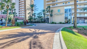 Een hotelingang met een met baksteen bestraat pad, palmbomen en een gebouw met de tekst 'STERRING BEACH'.