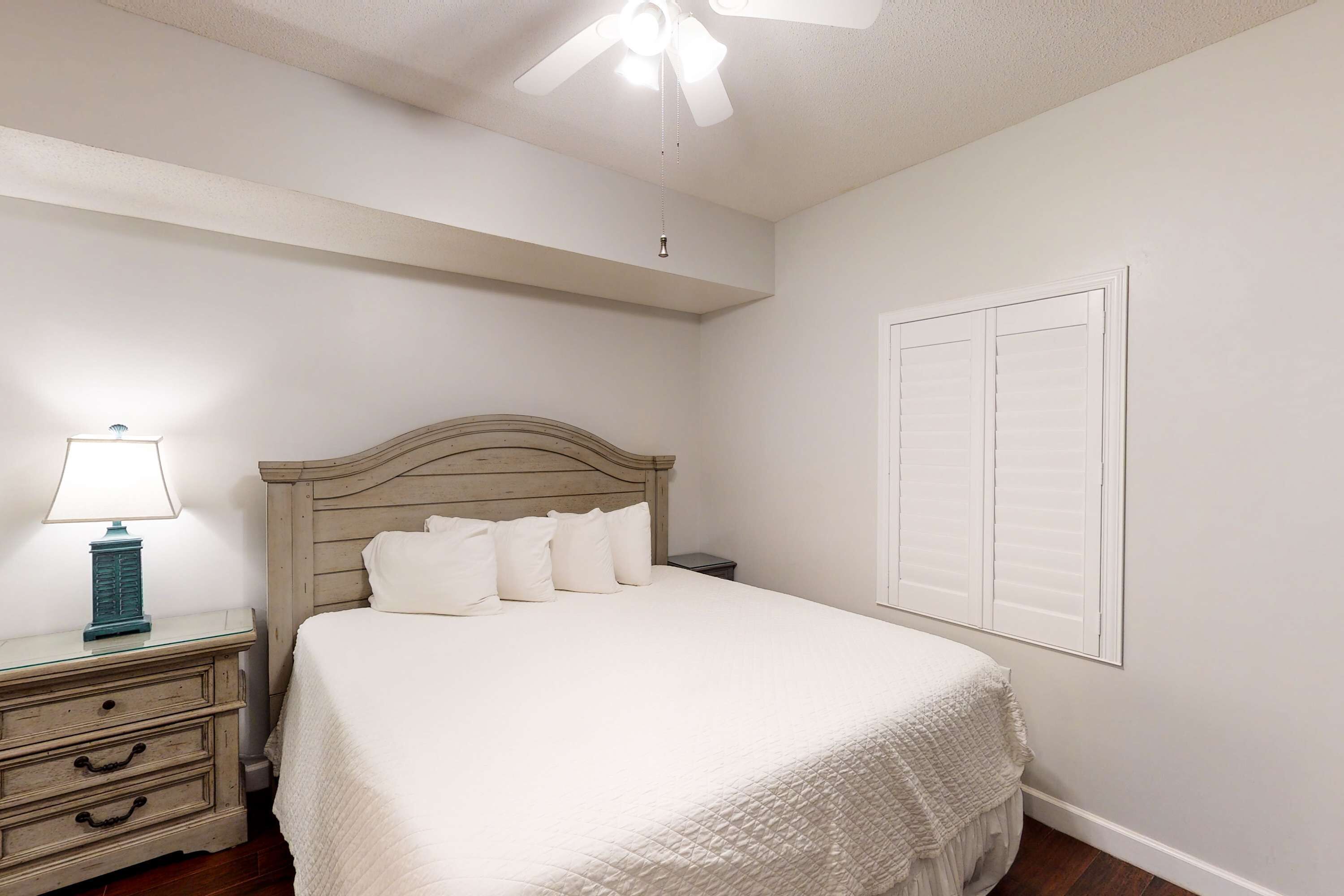 Un dormitorio con cama, mesita de noche, lámpara y ventilador de techo.