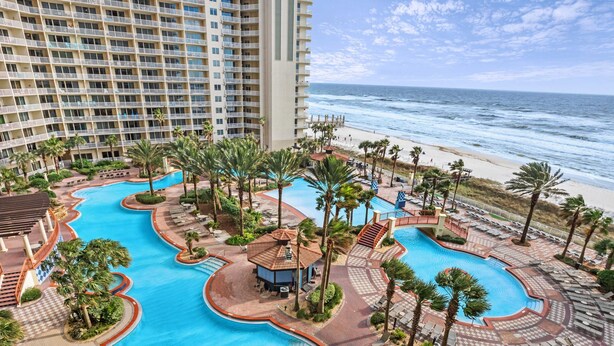 Een resort met meerdere zwembaden, een strand en een hoog gebouw.
