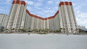 Een hoog hotel met een gebogen gevel, meerdere balkons en een ligging aan het strand.