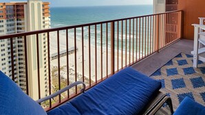 Een balkon met uitzicht op het strand en de oceaan, voorzien van blauwe kussens en een patroonrijk vloerkleed.