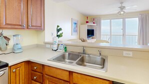 A kitchen with wooden cabinets, a double sink, a blender, and a window with curtains. - Beachfront 20th-floor condo with heated pools, hot tubs, balcony & Gulf views (Panama City Beach)