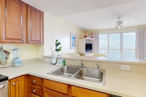 A kitchen with wooden cabinets, a double sink, a blender, and a window with curtains. - Beachfront 20th-floor condo with heated pools, hot tubs, balcony & Gulf views (Panama City Beach)