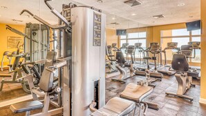 Un gimnasio con diversas máquinas de ejercicio, espejos y un amplio ventanal que proporciona luz natural.