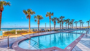Una piscina con solárium de baldosas, palmeras y vista al océano.