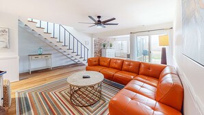 A spacious living room with a leather sofa, a round coffee table, and a staircase leading to another level. - Updated townhome with grassy yard, grill, open layout, W&D, & AC (Perdido Key)