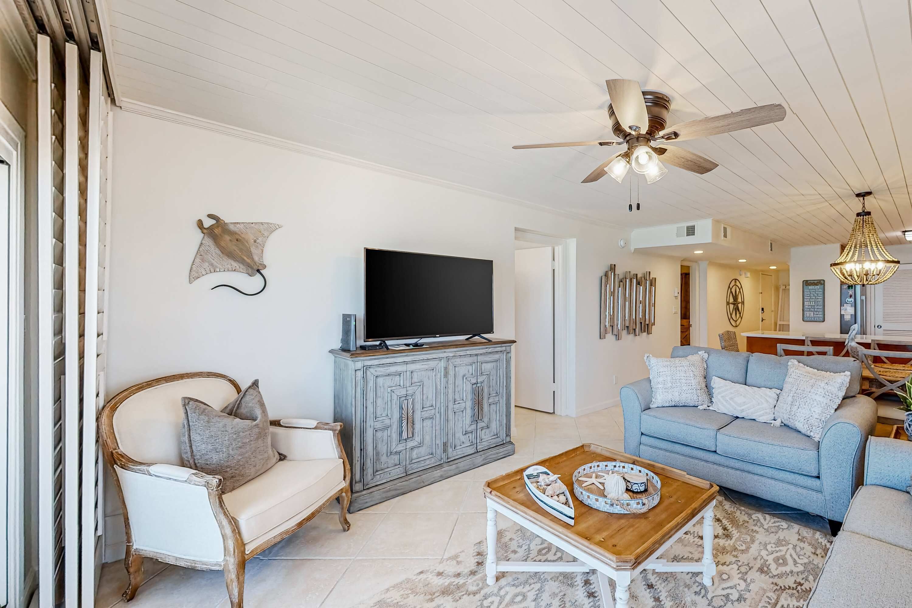 A living room with a television on a wooden cabinet, a ceiling fan, a light fixture, a blue sofa, and a white chair.