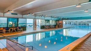 Una piscina interior con agua cristalina, rodeada de sillones de descanso y una zona de estar con mesas.