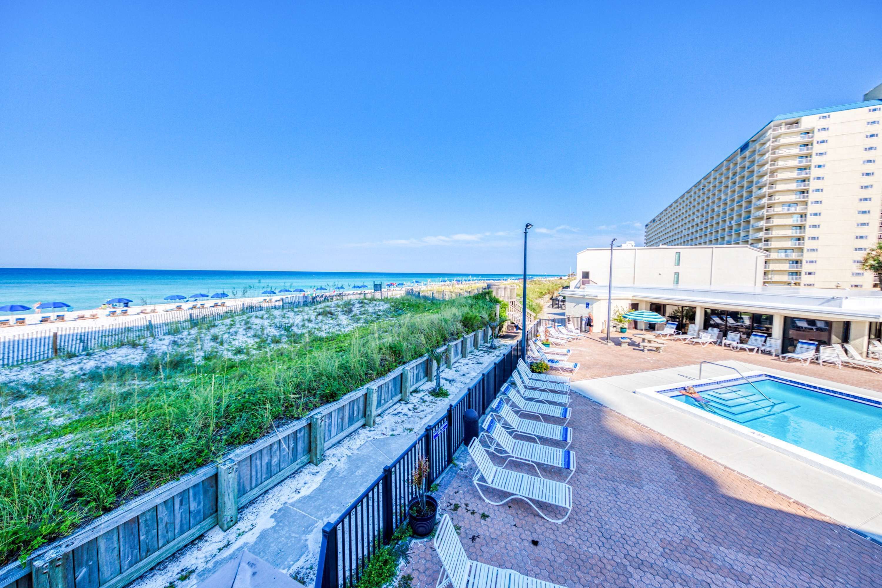 A hotel with a pool, beach view, and lounge chairs.