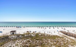 A beach with white sand, clear blue water, and a wooden boardwalk leading to a small building. - Stunning third-floor condo with balcony, washer&dryer & pool (Destin)