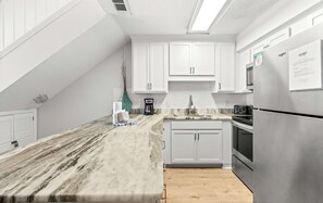 A modern kitchen with white cabinets, a marble countertop, a built-in oven, and a stainless steel refrigerator. - Stunning third-floor condo with balcony, washer&dryer & pool (Destin)