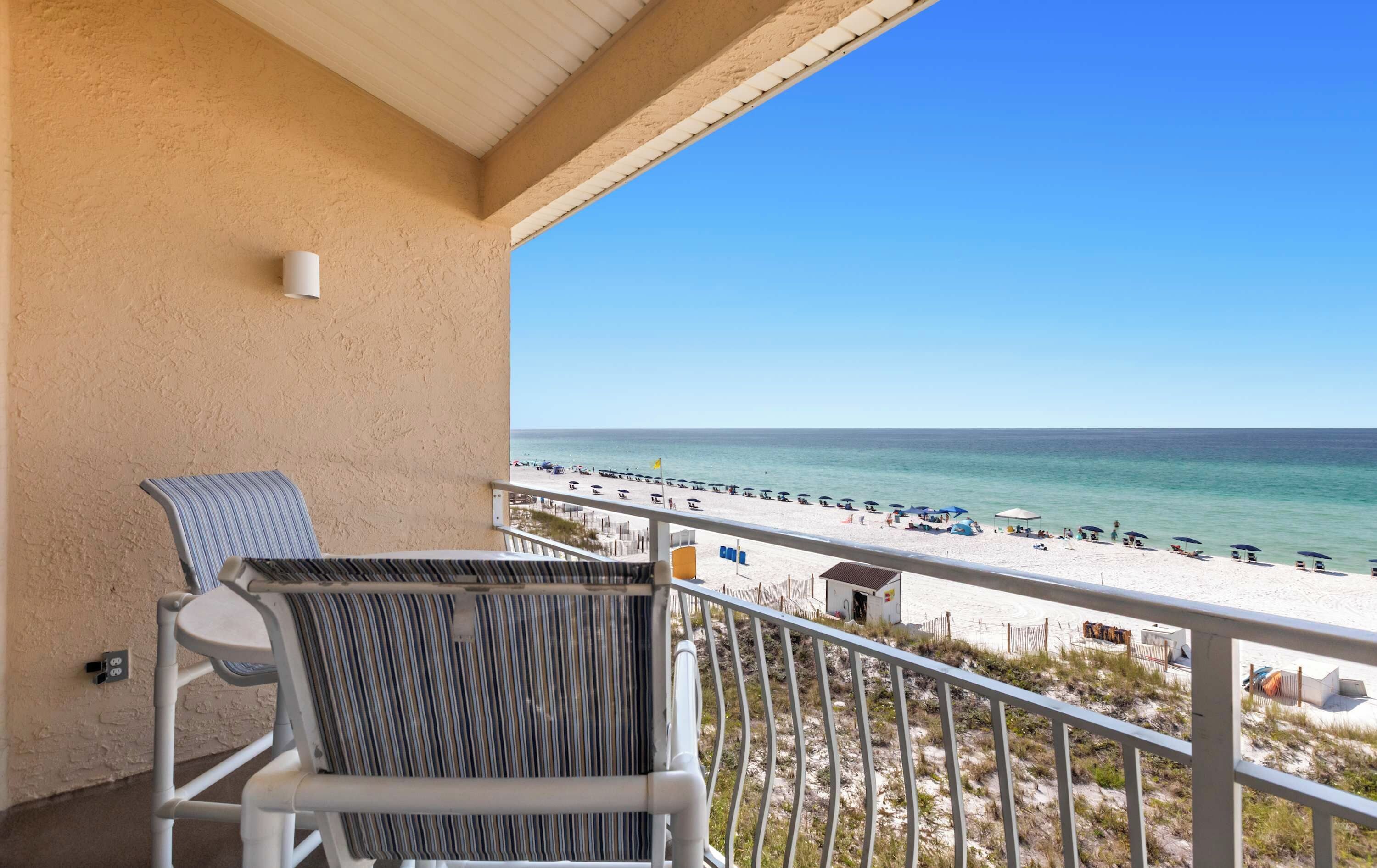 A balcony with a view of a beach, a chair, and a railing.