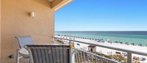 A balcony with a view of a beach, a chair, and a railing.