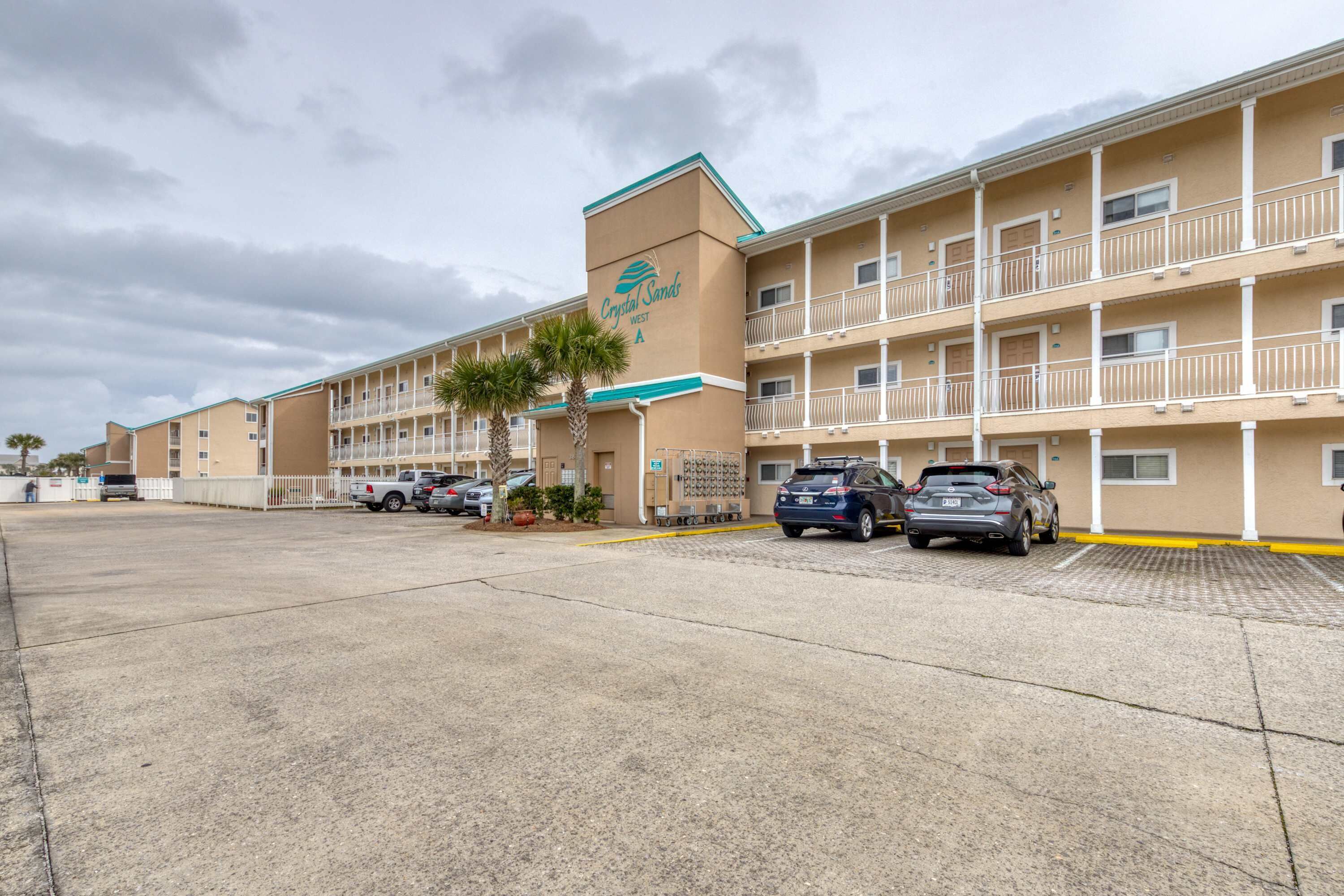 A hotel with a central entrance, multiple balconies, and a parking lot.