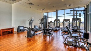 A spacious gym with various exercise machines, large windows, and a wooden floor. - Gulf-front condo with balcony, beach access, hot tub, pool & gym (Panama City Beach)