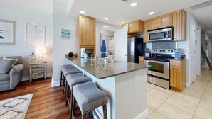 A modern kitchen with a central island, wooden cabinets, stainless steel appliances, and a bar stool seating area. - Gulf-front condo with balcony, beach access, hot tub, pool & gym (Panama City Beach)