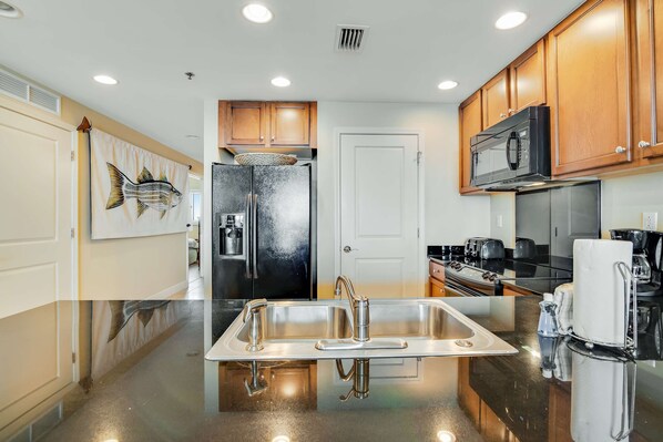 A modern kitchen with stainless steel appliances, a double sink, and wooden cabinets. - Beautiful condo with all the comforts of home | Pool | Hot tub (Panama City Beach)