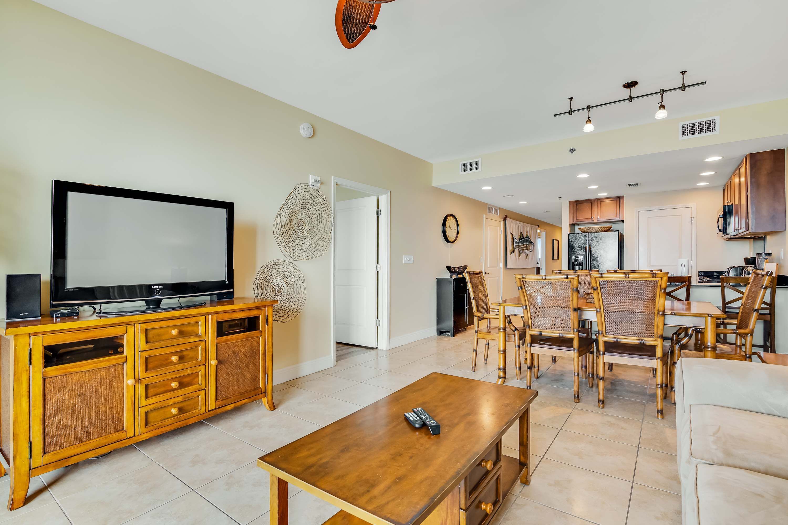 A modern living room with a TV, wooden entertainment unit, and a dining area with bamboo chairs.
