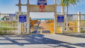 Ein Zugangstor zum Strand mit Schildern, die angeben, dass keine Badeaufsicht vorhanden ist, Glasbehälter verboten sind und vor gefährlichen Meerestieren gewarnt wird.